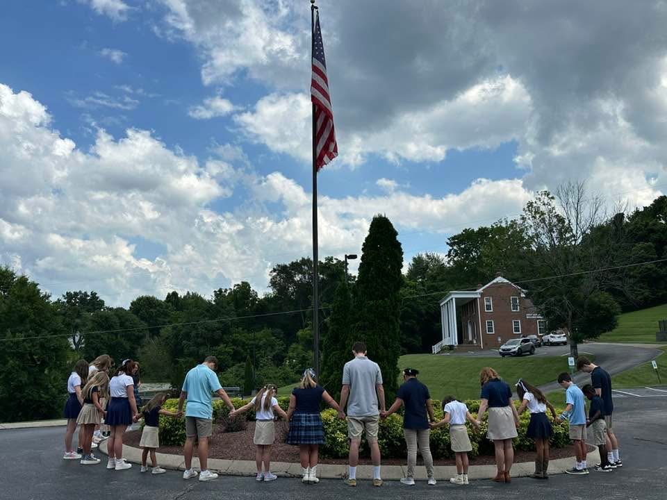 Students holding hands in prayer around the American flag at Safe Harbor Hybrid